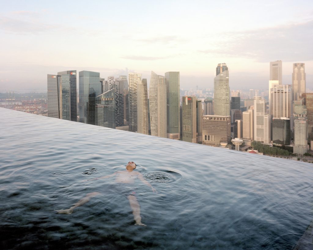 A man floats in the 57th-floor swimming pool of the Marina Bay Sands Hotel, with the skyline of the Singapore financial district behind him. 2013 Paolo Woods & Gabriele GalimbertiÑINSTITUTE